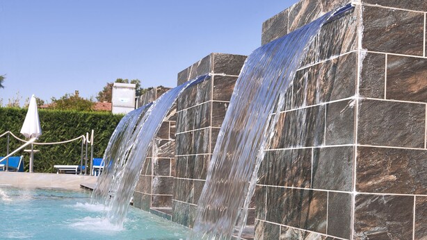 Una piscina con cascada, agua cristalina azul y pared de azulejos.
