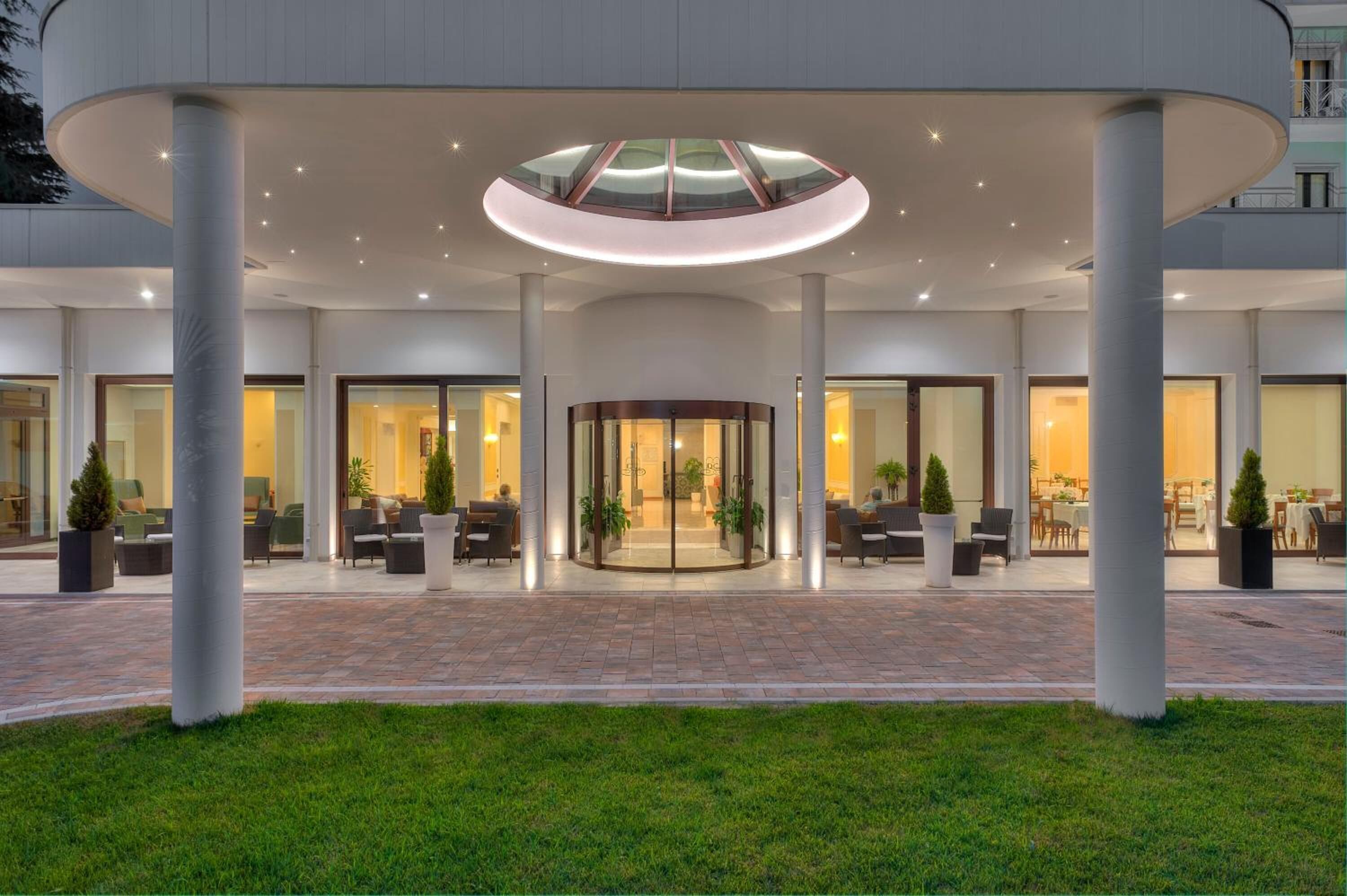 A modern hotel entrance with a circular glass ceiling, large columns, and a paved courtyard.
