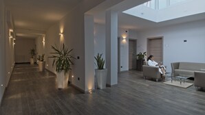 Un interior amplio y moderno con un largo pasillo, plantas en macetas, una zona de estar con una mesa de vidrio y un tragaluz.