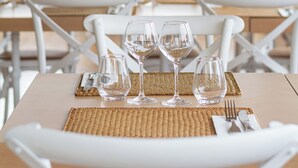 Un restaurante con sillas y mesas blancas, cada juego con un posavasos, tenedor y cuchillo.
