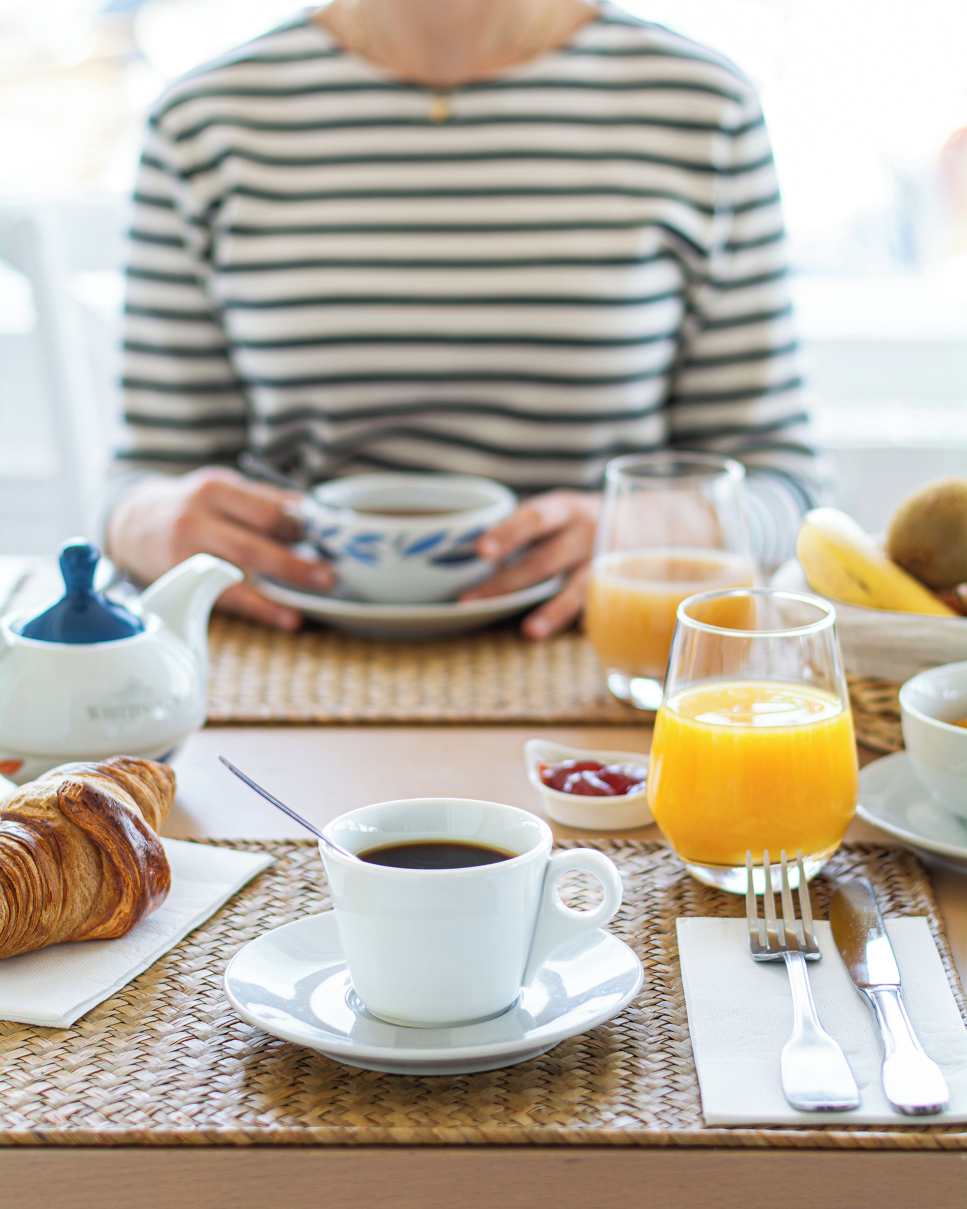 A breakfast setting with croissants, coffee, orange juice, and a teapot on a woven placemat.