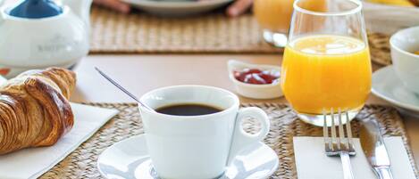 A breakfast setting with croissants, coffee, orange juice, and a teapot on a woven placemat.