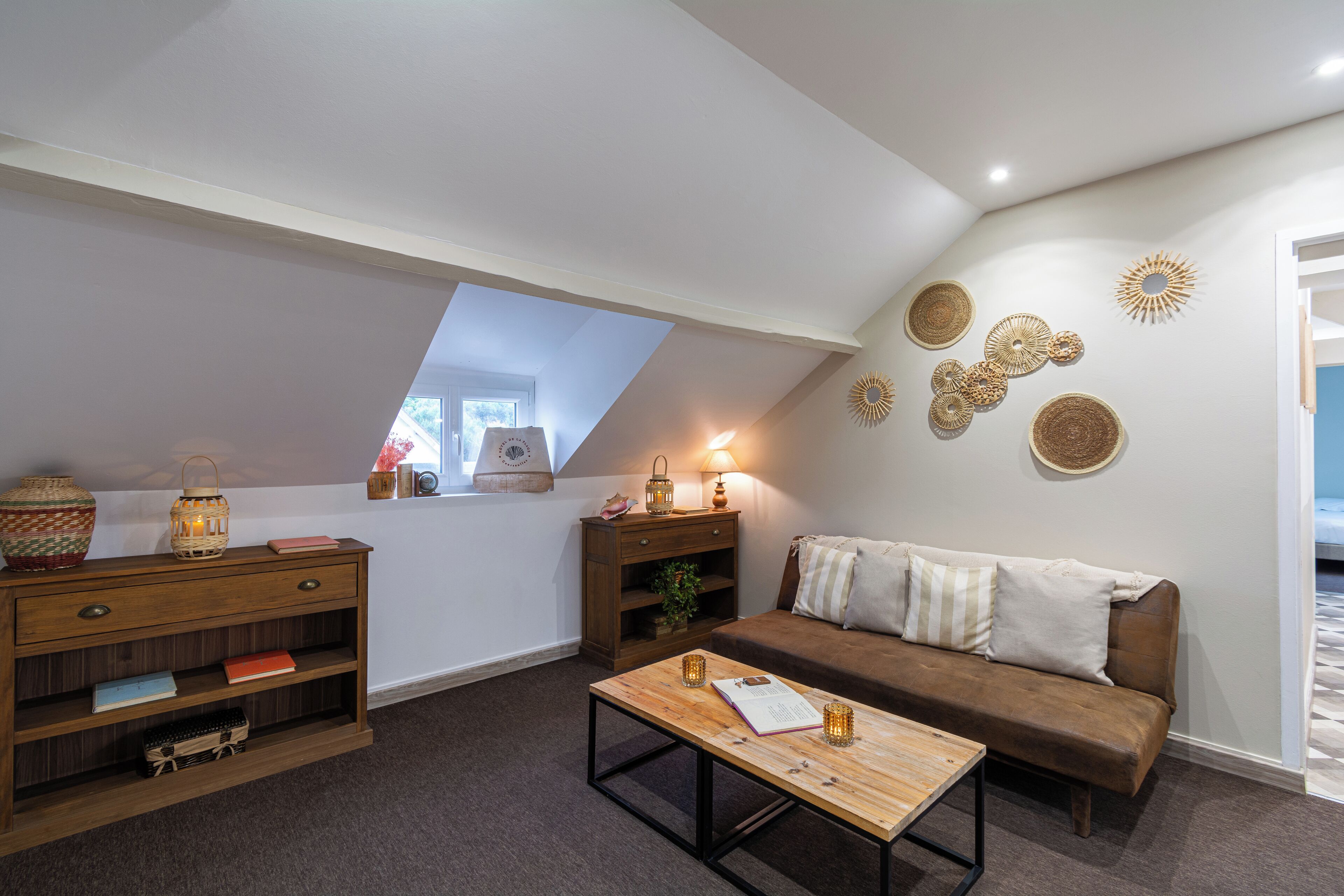 A cozy loft bedroom with a sloped ceiling, a wooden dresser, a brown sofa, and decorative wall art.