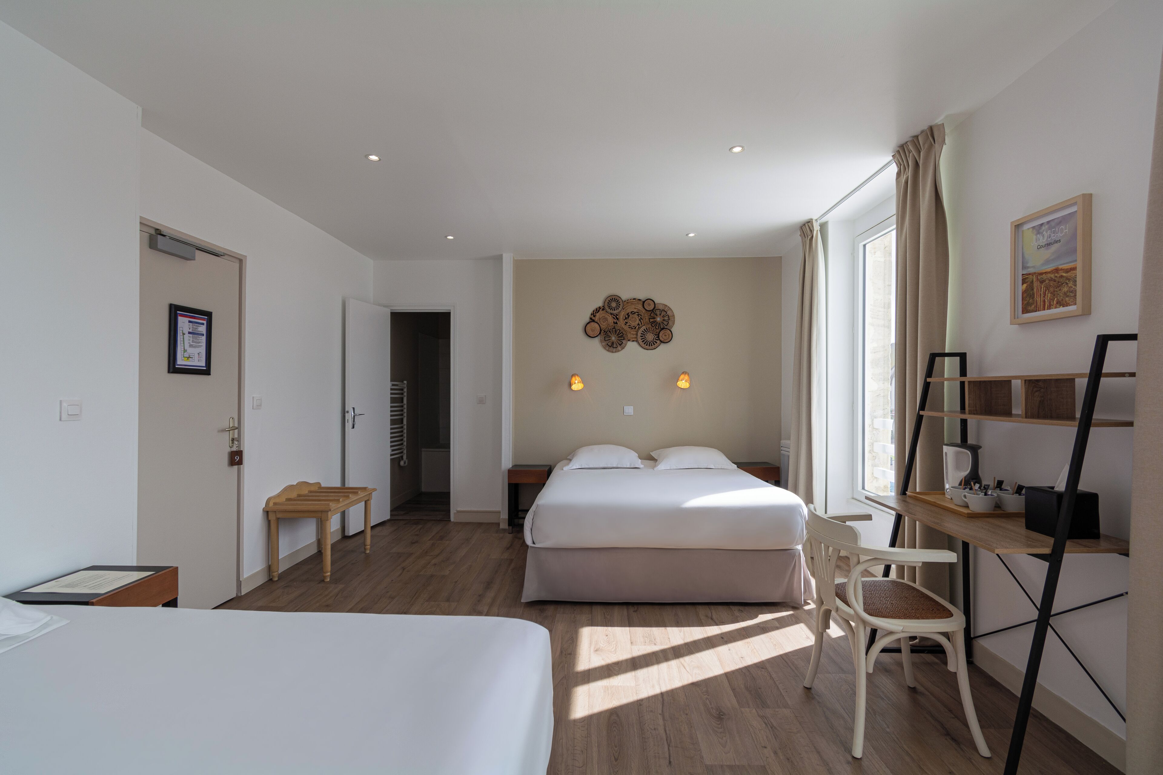 Una habitación de hotel con cama, escritorio, silla, una mesita y un estante en la pared.