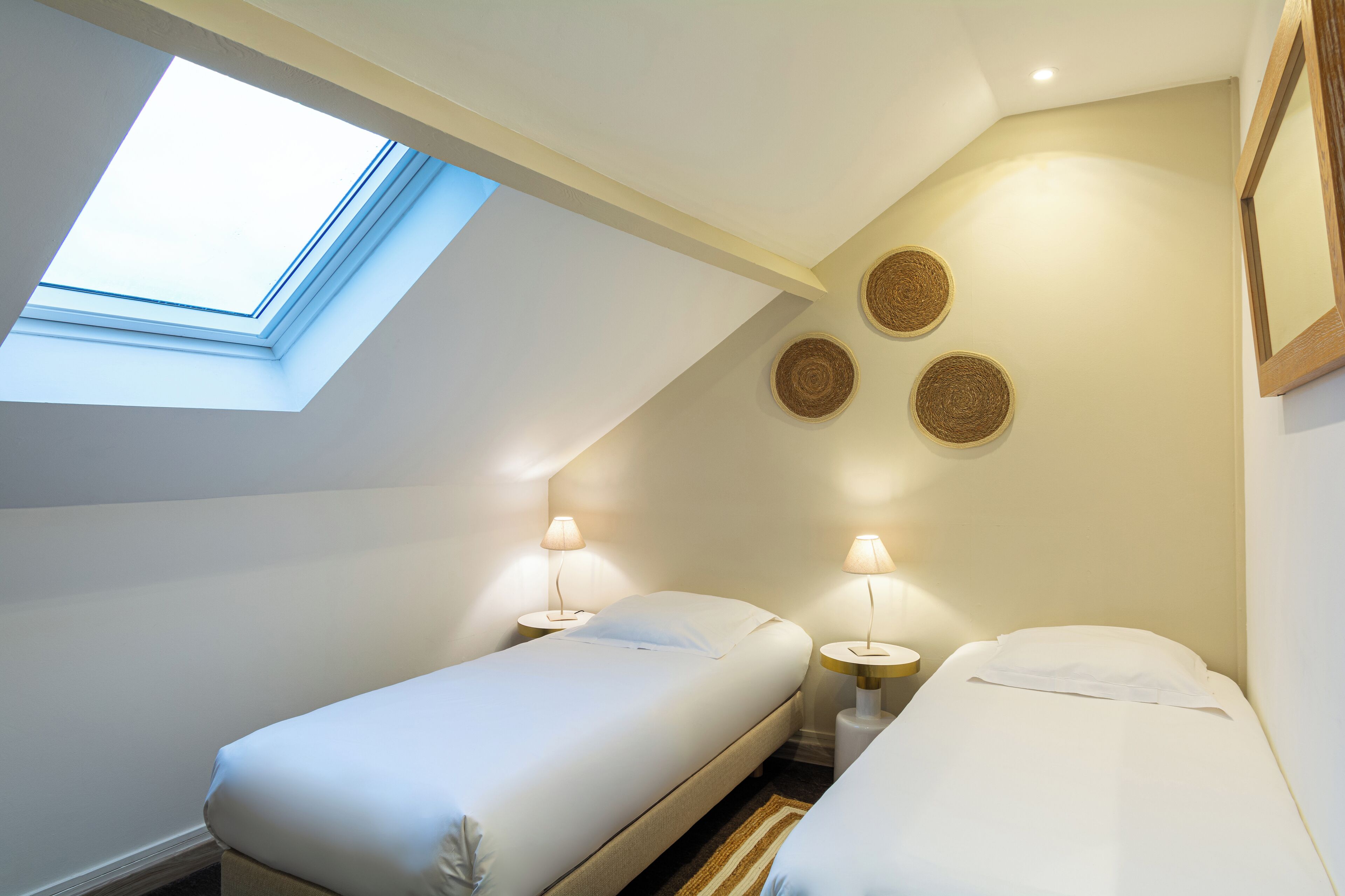 Un dormitorio pequeño y luminoso con dos camas, un tragaluz y decoración en las paredes.