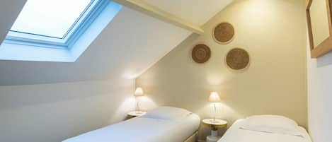 Un dormitorio pequeño y luminoso con dos camas, un tragaluz y decoración en las paredes.