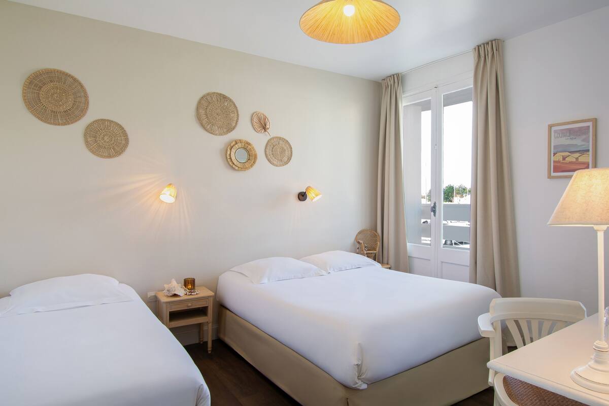 A hotel room with two beds, a small table, a chair, and decorative wall hangings.