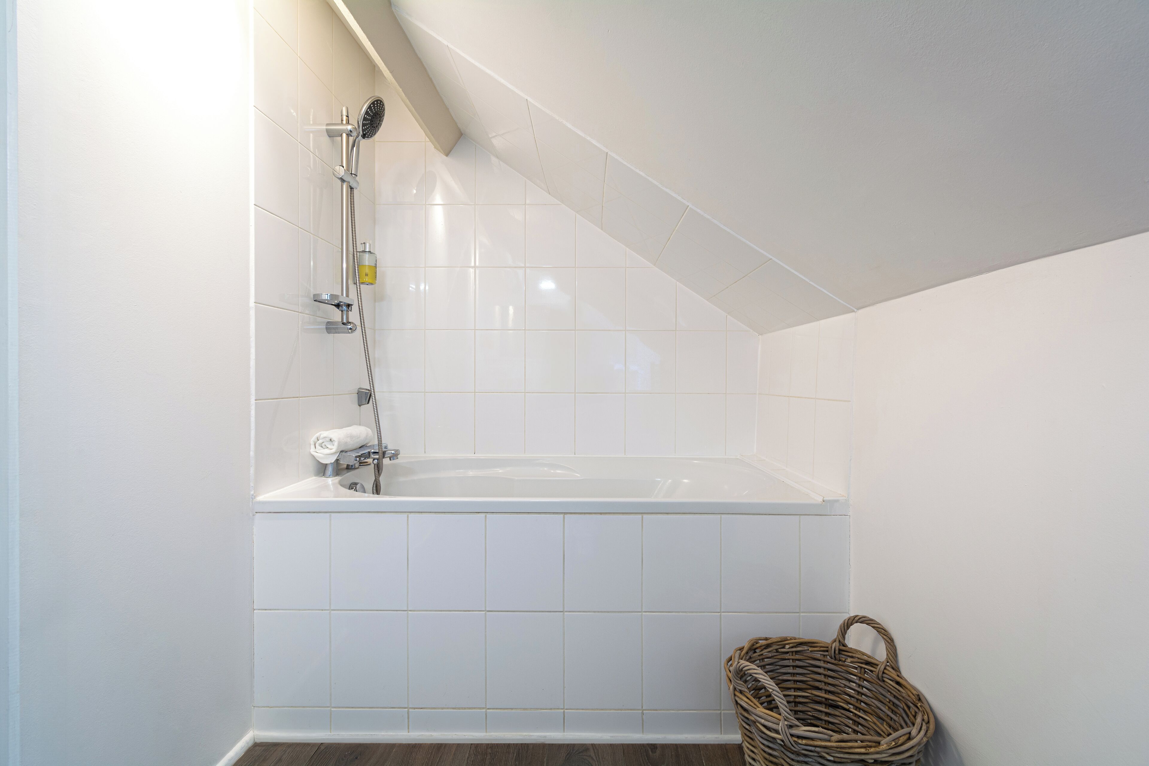 Un bagno con una vasca da bagno bianca, una doccia e un cesto in vimini.