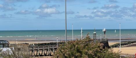 Vista costera con muelle de madera, cielo despejado y el océano al fondo.