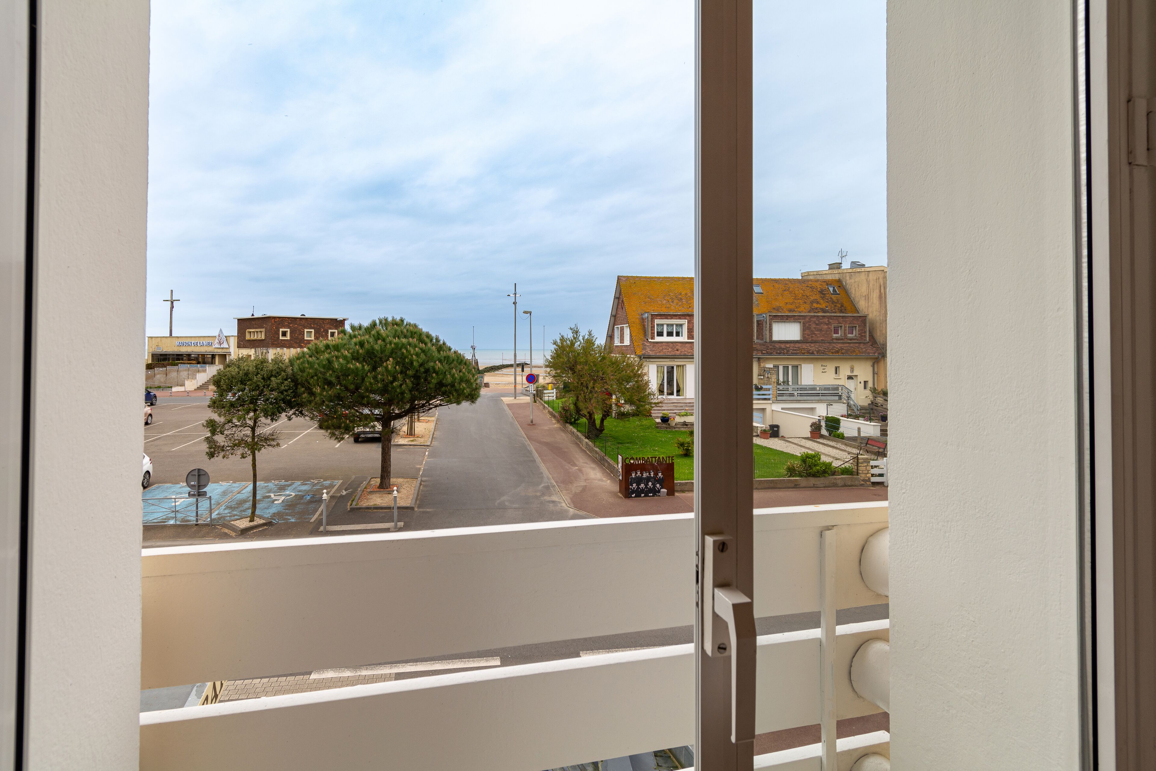 Une vue depuis un balcon donnant sur une rue bordée d’immeubles et d’arbres, avec un ciel dégagé.