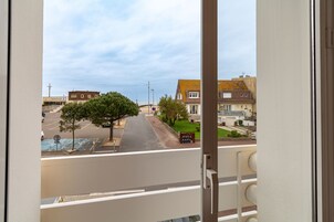 Vista desde un balcón con vista a una calle con edificios, árboles y cielo despejado.