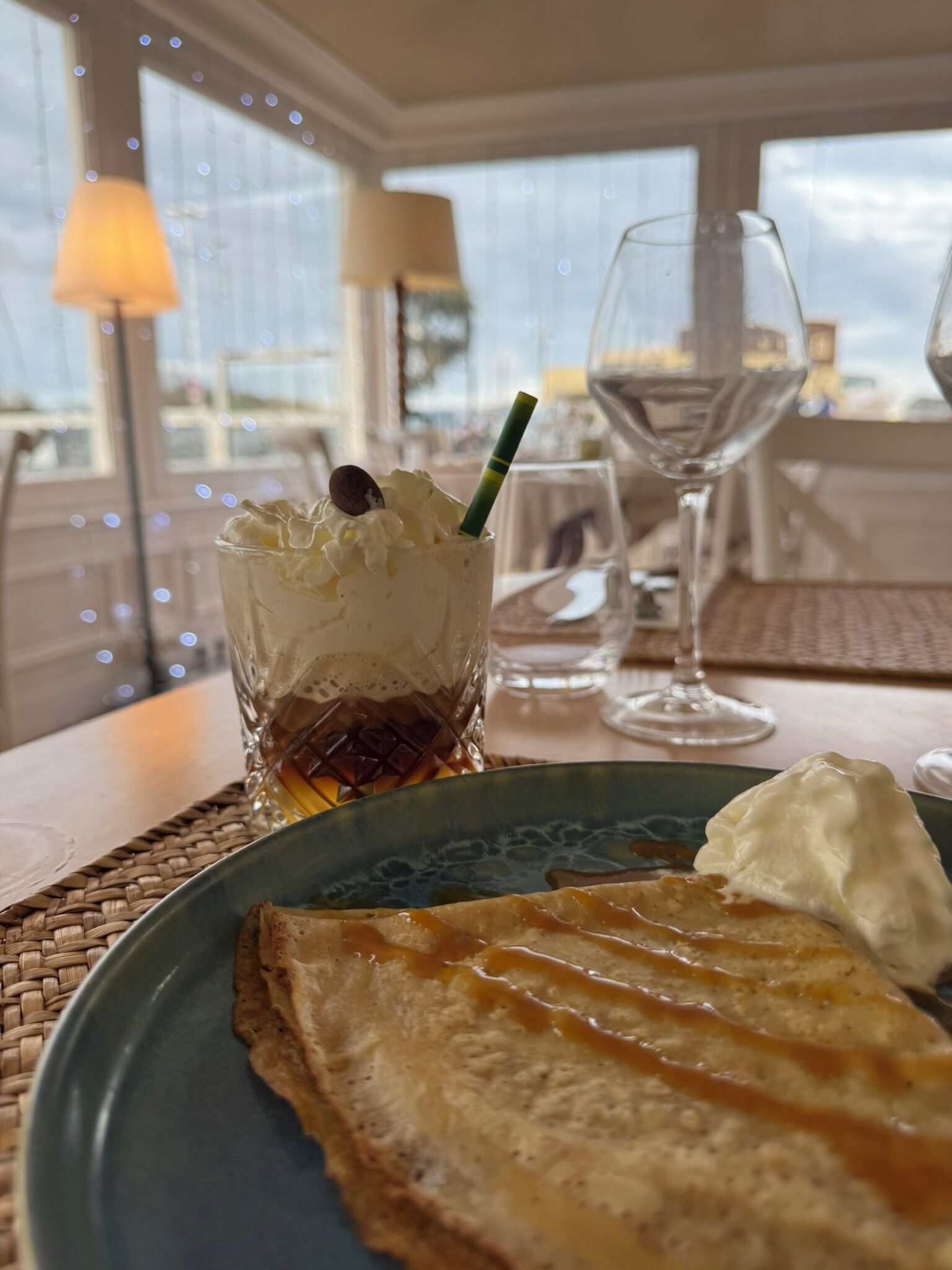 Ein Dessertteller mit einer Crêpe und einem Glas cremiger Flüssigkeit, möglicherweise Kaffee oder Tee, mit einem Strohhalm.