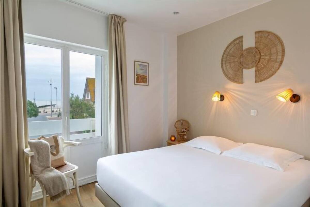 A hotel room with a bed, a chair, a window with curtains, and wall-mounted lights.