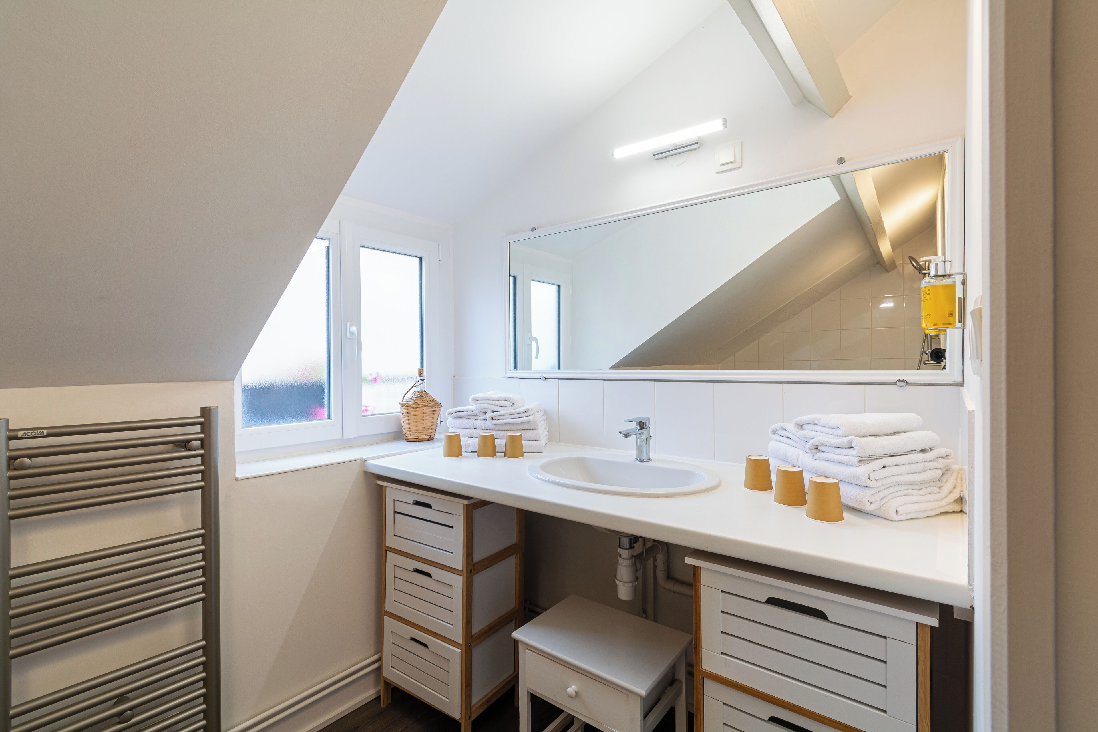 A modern bathroom with a skylight, a large mirror, a white sink, and neatly folded towels.