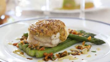 A plate with a piece of fish, asparagus, and a garnish of nuts and herbs.