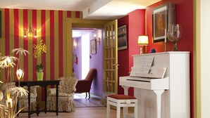 Una habitación con un piano, una mesa con sillas, una lámpara y un florero con flores.