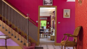 Una escalera con barandilla de madera y una pared roja. Se ve una silla y una mesa con libros.