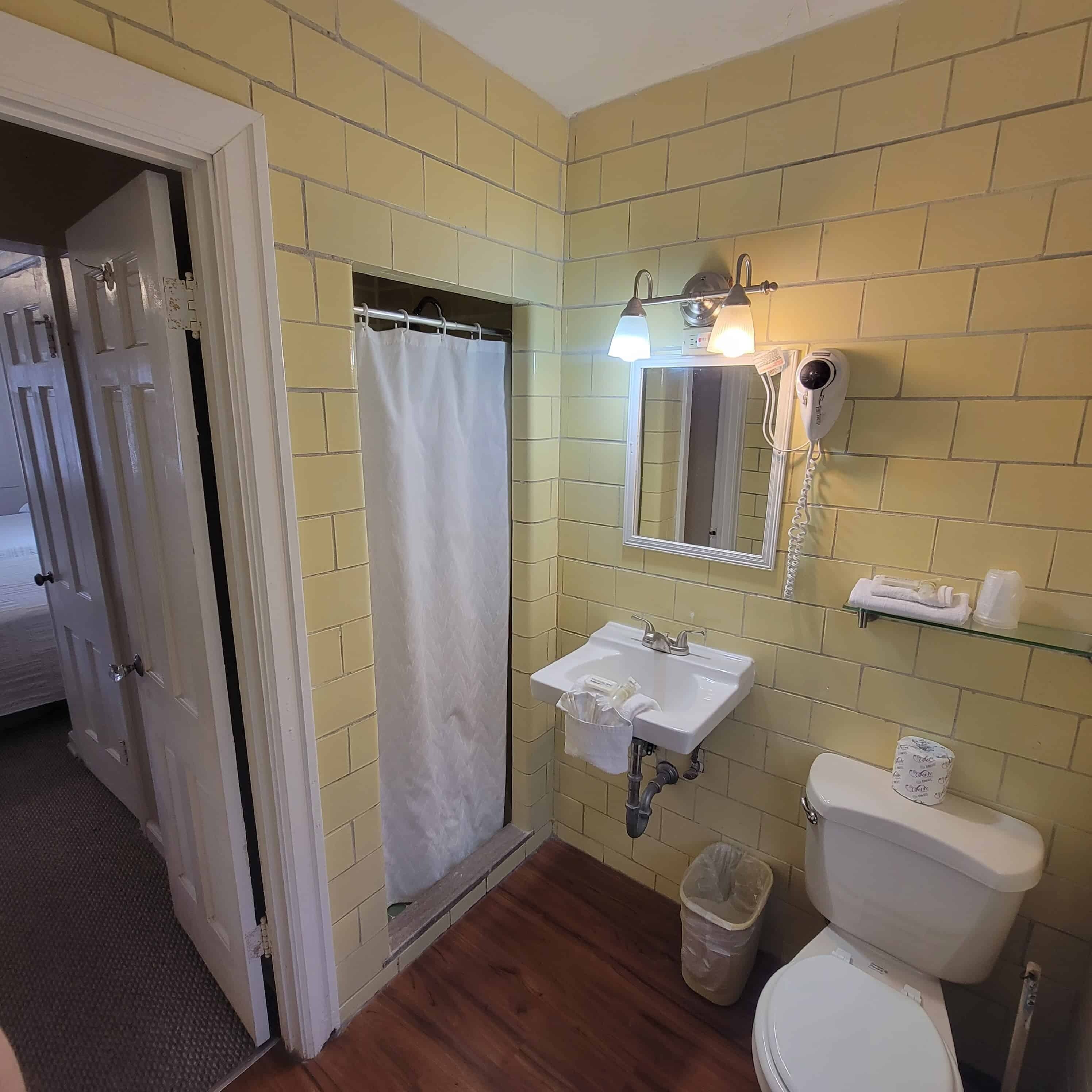 Un baño con paredes de ladrillo amarillo, un lavamanos blanco, un espejo, una cortina de ducha y un inodoro.