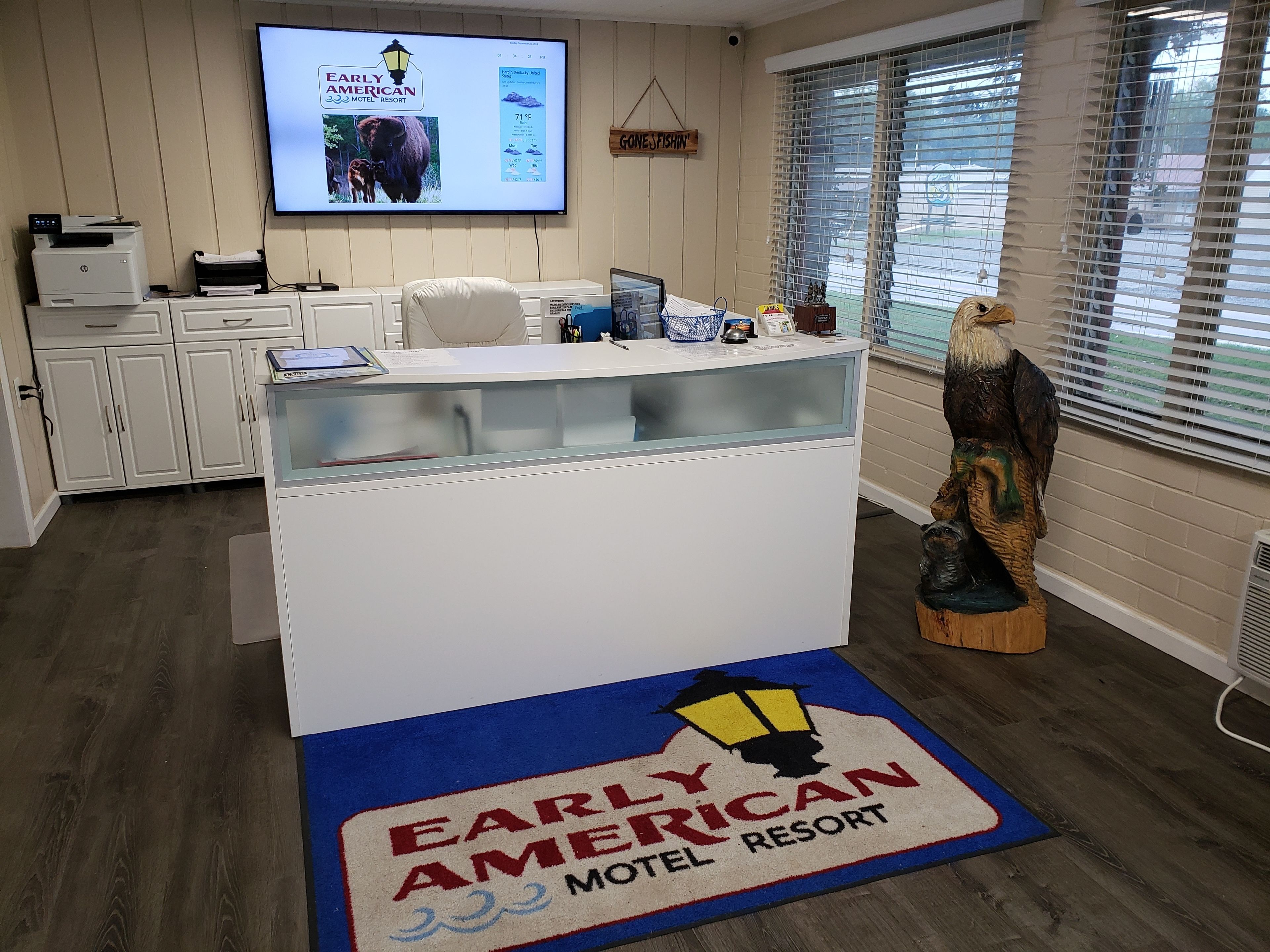 Een receptiebalie bij het Early American Motel & Resort, met een groot scherm waarop de naam van het hotel en de faciliteiten staan.
