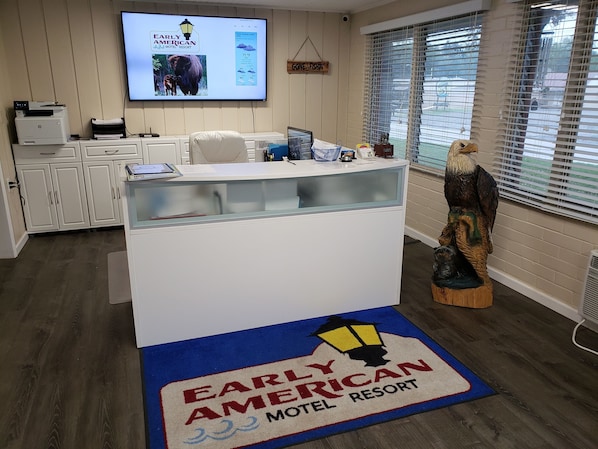 Mostrador de recepción del Early American Motel & Resort con una pantalla grande que muestra el nombre y los servicios del hotel.