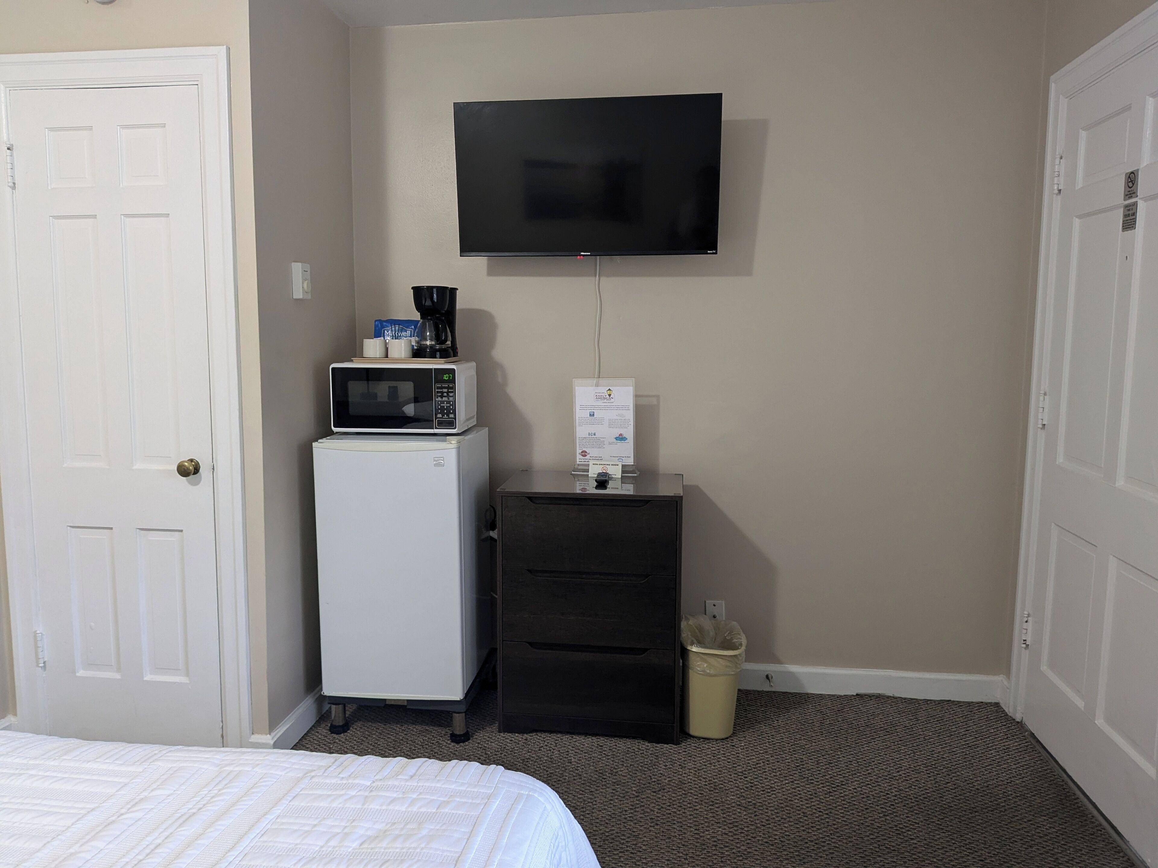 Habitación de hotel con cama, microondas, refrigerador, televisión, basurero y un mueble pequeño.