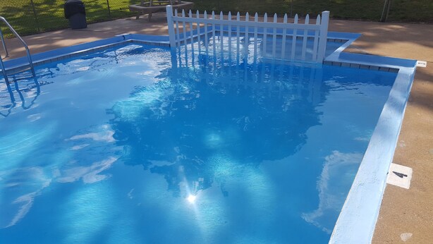 A clear blue swimming pool with a white fence, surrounded by a concrete deck. - Early American Motel (Hardin)
