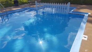 A clear blue swimming pool with a white fence, surrounded by a concrete deck.