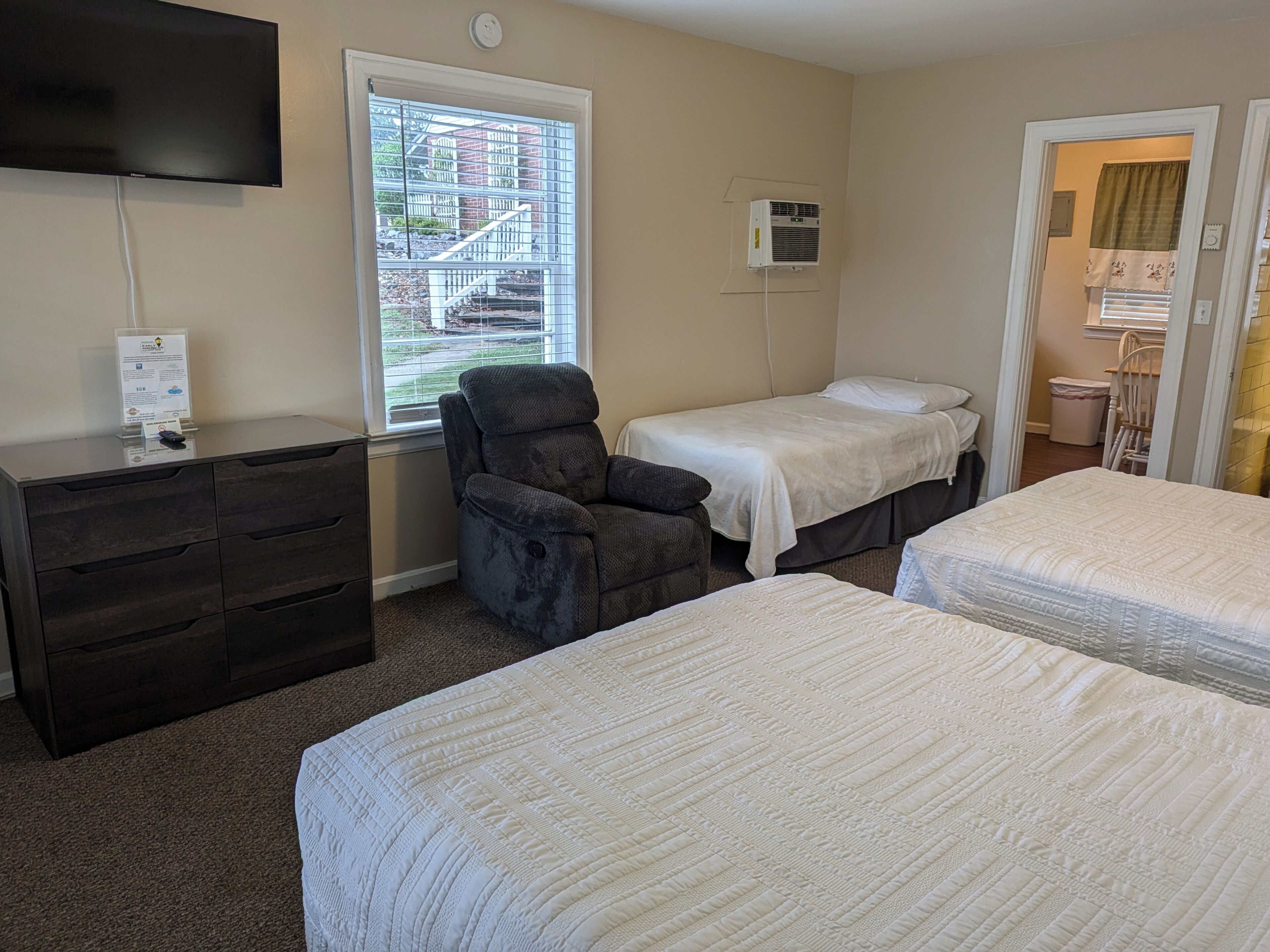 A hotel room with two beds, a desk, a chair, a TV, and a window with a view of a building.