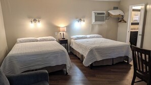 A hotel room with two beds, a chair, a nightstand, a lamp, and a wardrobe. - Early American Motel (Hardin)