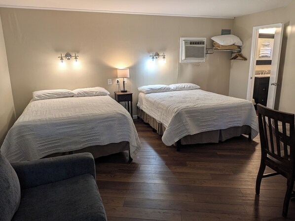 A hotel room with two beds, a chair, a nightstand, a lamp, and a wardrobe.