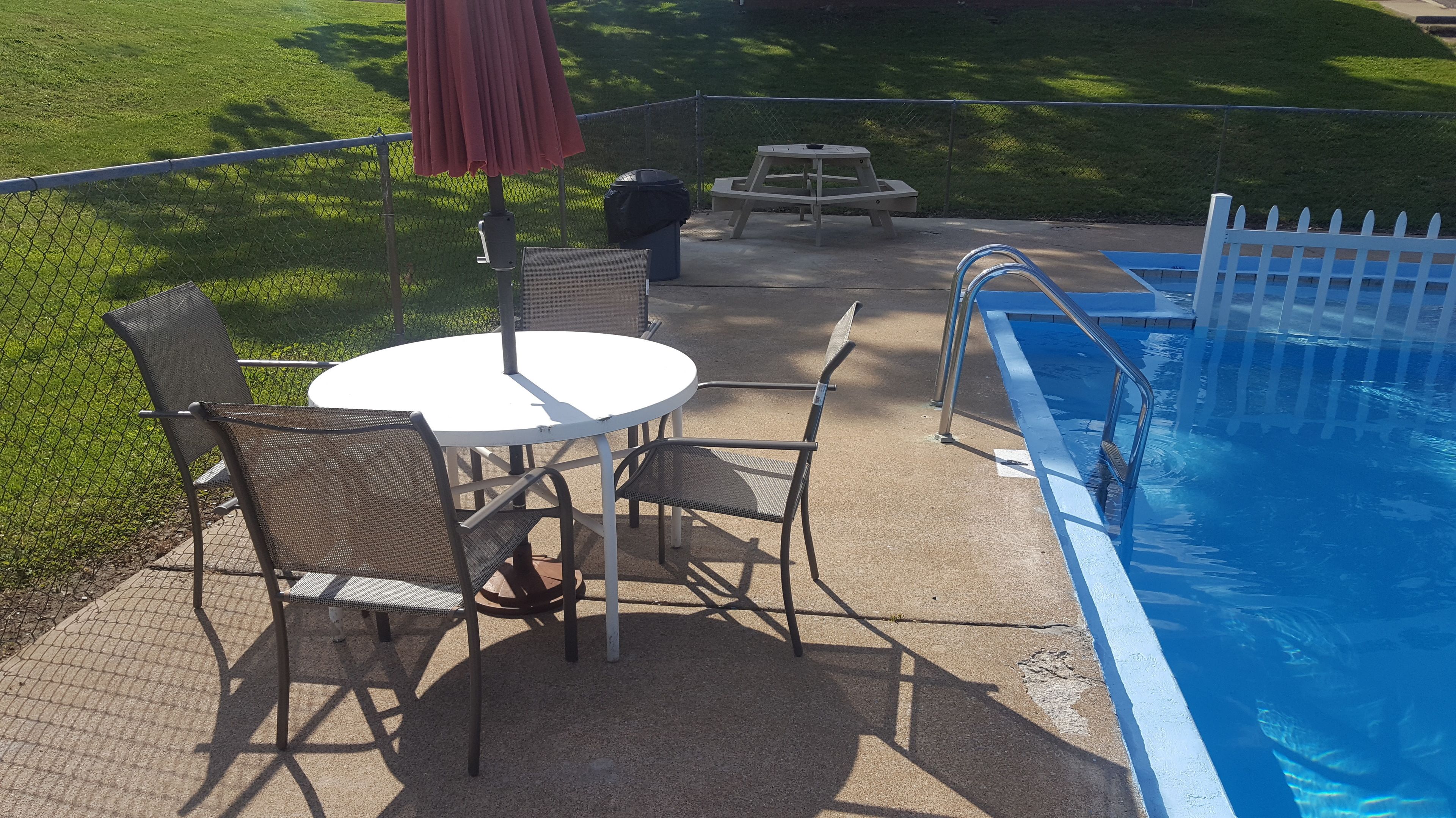 Un espace aménagé au bord de la piscine, avec une table et des chaises, un parasol et une poubelle.