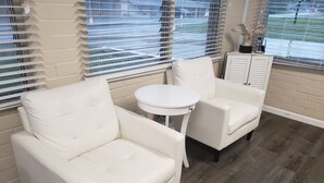 A room with a white leather sofa, a small round table, and a white armchair. - Early American Motel (Hardin)