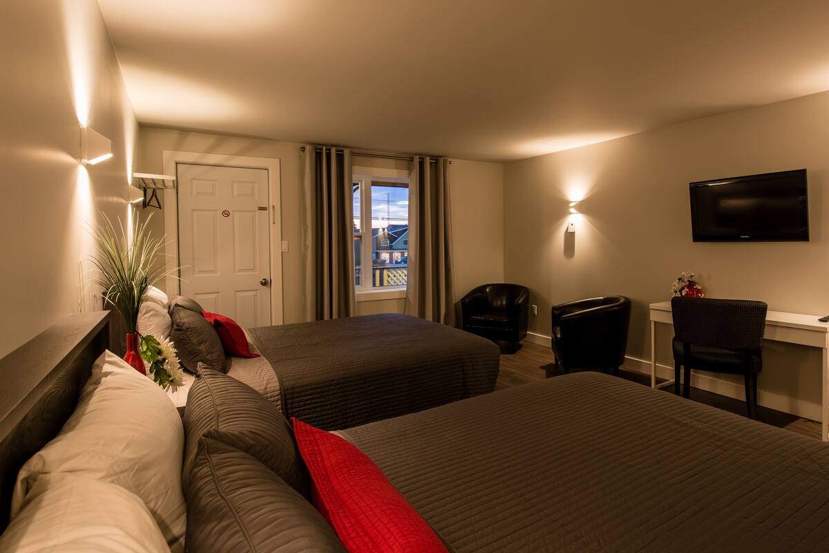 Una habitación de hotel con dos camas, un escritorio, una silla, un televisor y una puerta.