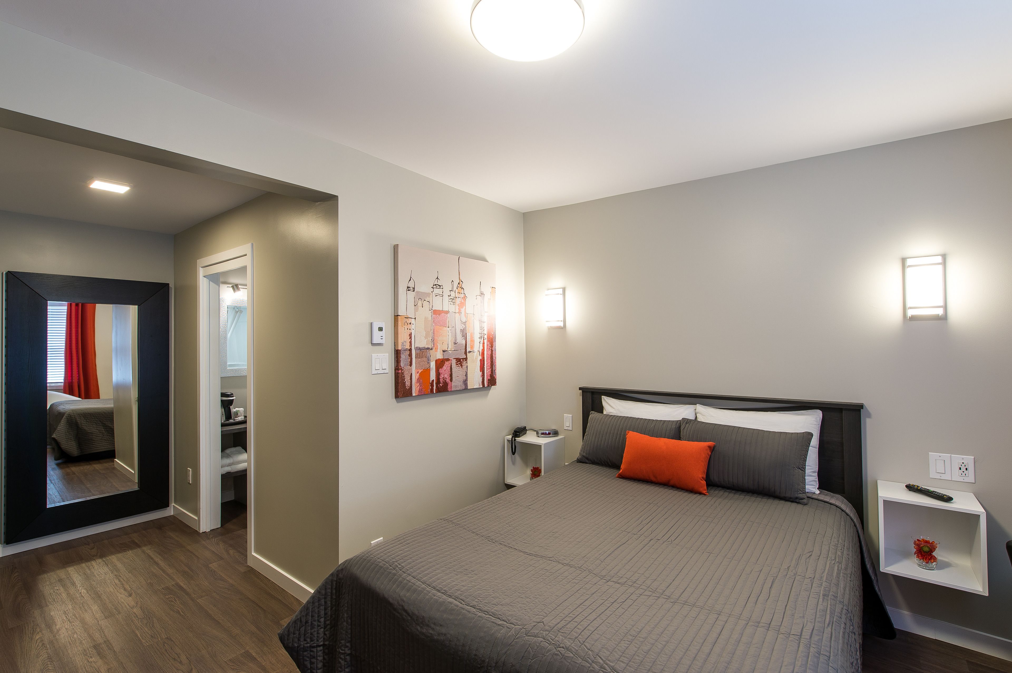 Una habitación de hotel moderna con una cama grande, una mesita de noche, un cuadro colgado en la pared y una puerta que da a un baño.