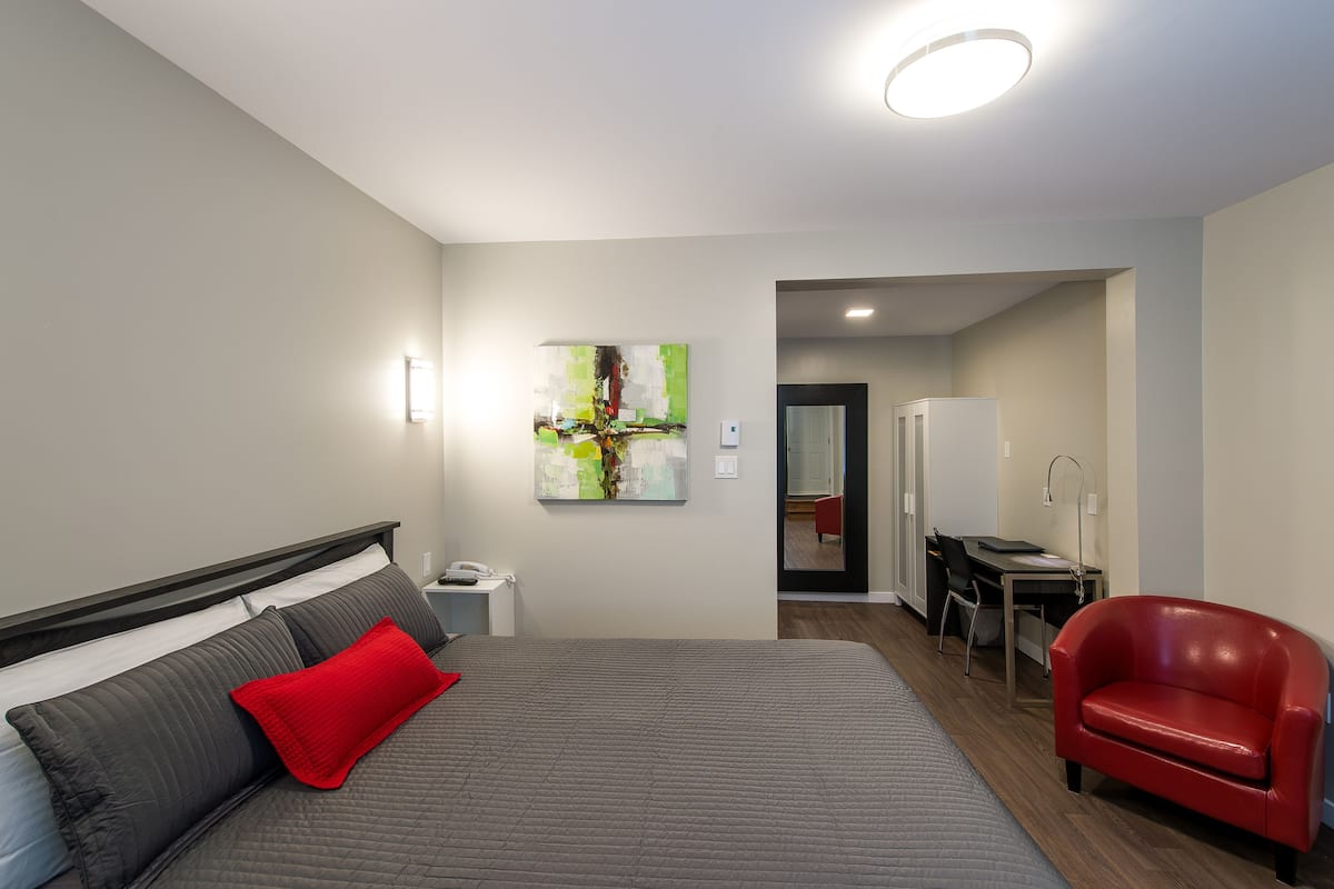 Una habitación de hotel moderna con una cama grande, una silla roja, un escritorio y un cuadro en la pared.