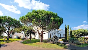 A white building with a large tree in front, a sign for a hotel, and a clear blue sky.