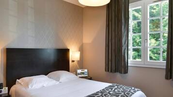 Una habitación de hotel con cama, mesita de noche, lámpara, ordenador portátil y ventana con cortinas.