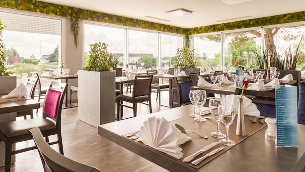 A restaurant with tables set for dining, large windows, and indoor plants.