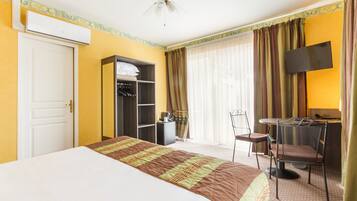 Habitació d'hotel amb un llit, un armari, una taula de nit amb cadira, una televisió i un ventilador de sostre.