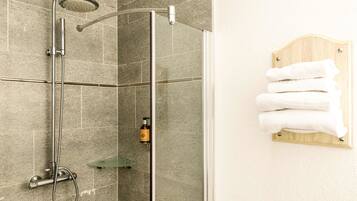 Une douche avec une porte en verre, un porte-serviettes avec des serviettes pliées et un flacon de shampoing accroché au mur.
