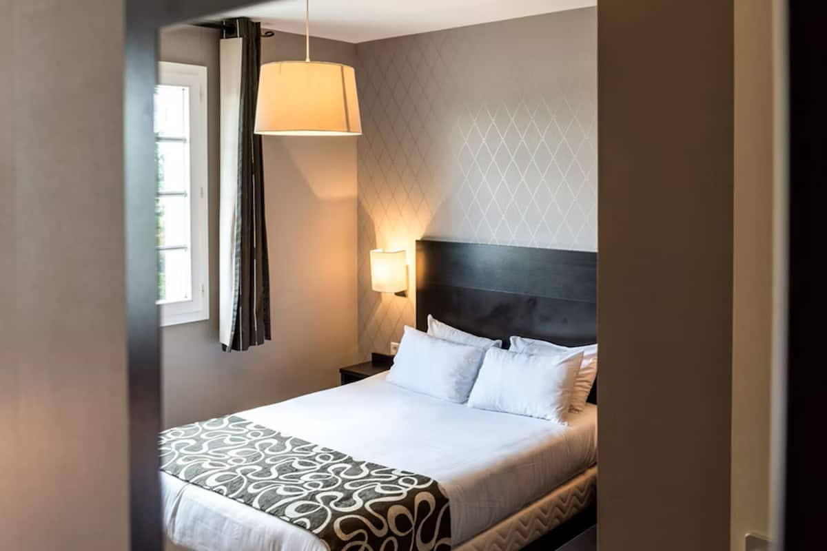 A hotel room with a bed, a nightstand, a lamp, and a window with curtains.