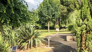 A garden pathway with a solar-powered light post, surrounded by lush greenery and trees.