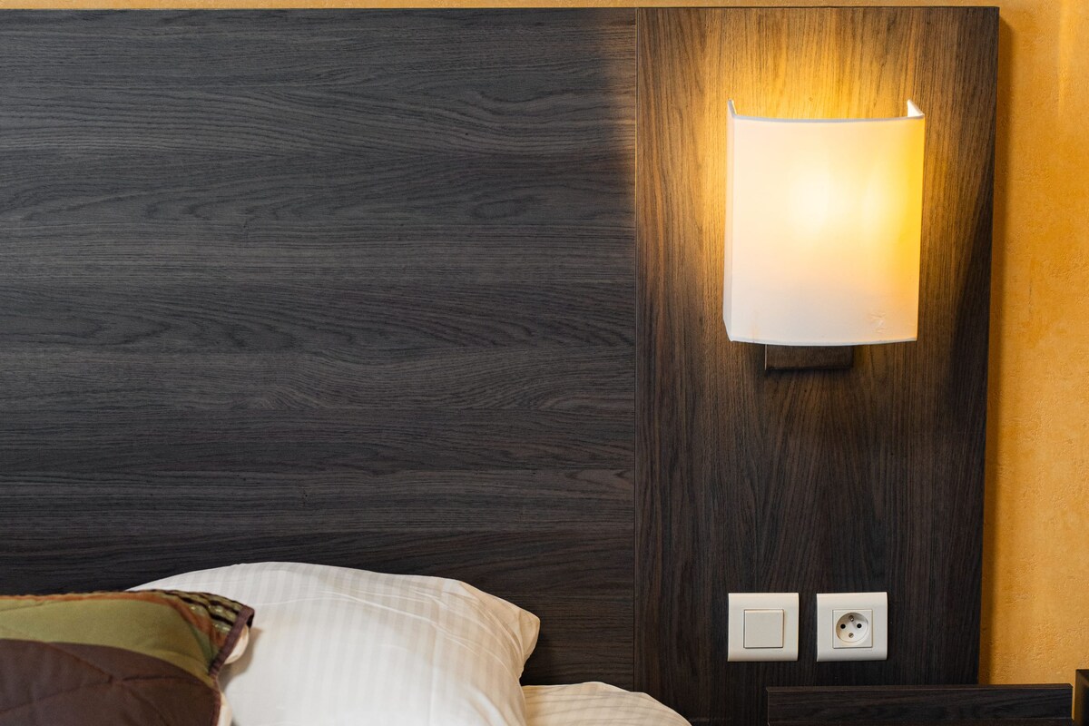 A neatly made bed with pillows, a bedside table, and a wall-mounted light fixture.