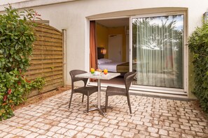 A small patio with a table and chairs, a sliding glass door leading to a bedroom, and a wooden fence.