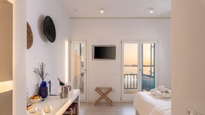 Ein Hotelzimmer mit einem Bett, einem an der Wand befestigten Fernseher, einem kleinen Tisch mit Vase und Früchten sowie einem Balkon mit Aussicht.