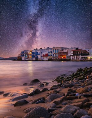 A coastal town at night with a starry sky, featuring colorful buildings and a calm sea.