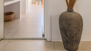 Ein modernes Interieur mit einer großen Steinvase, getrockneten Pflanzen, einem Korbwägelchen und einer minimalistischen Sitzecke.
