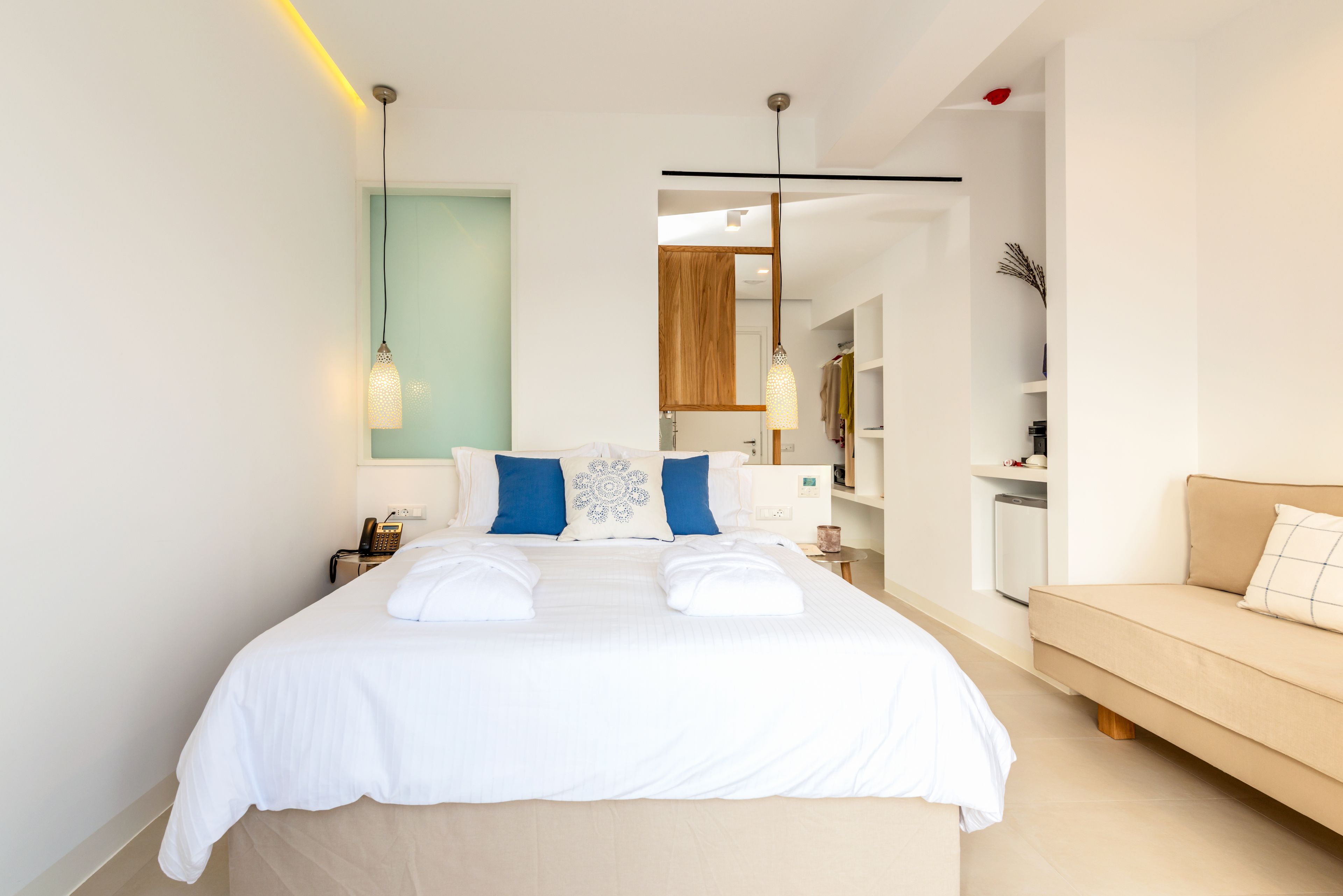 Una habitación de hotel moderna con una cama grande, mesitas de noche, un armario y un sofá.