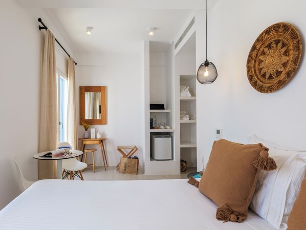 A modern hotel room with a bed, a desk, a chair, a small table, a mirror, a wardrobe, and a hanging light fixture.