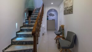 Ein modernes Interieur mit einer Marmortreppe, einem Holzgeländer und einer Sitzecke mit gemusterten Stühlen.